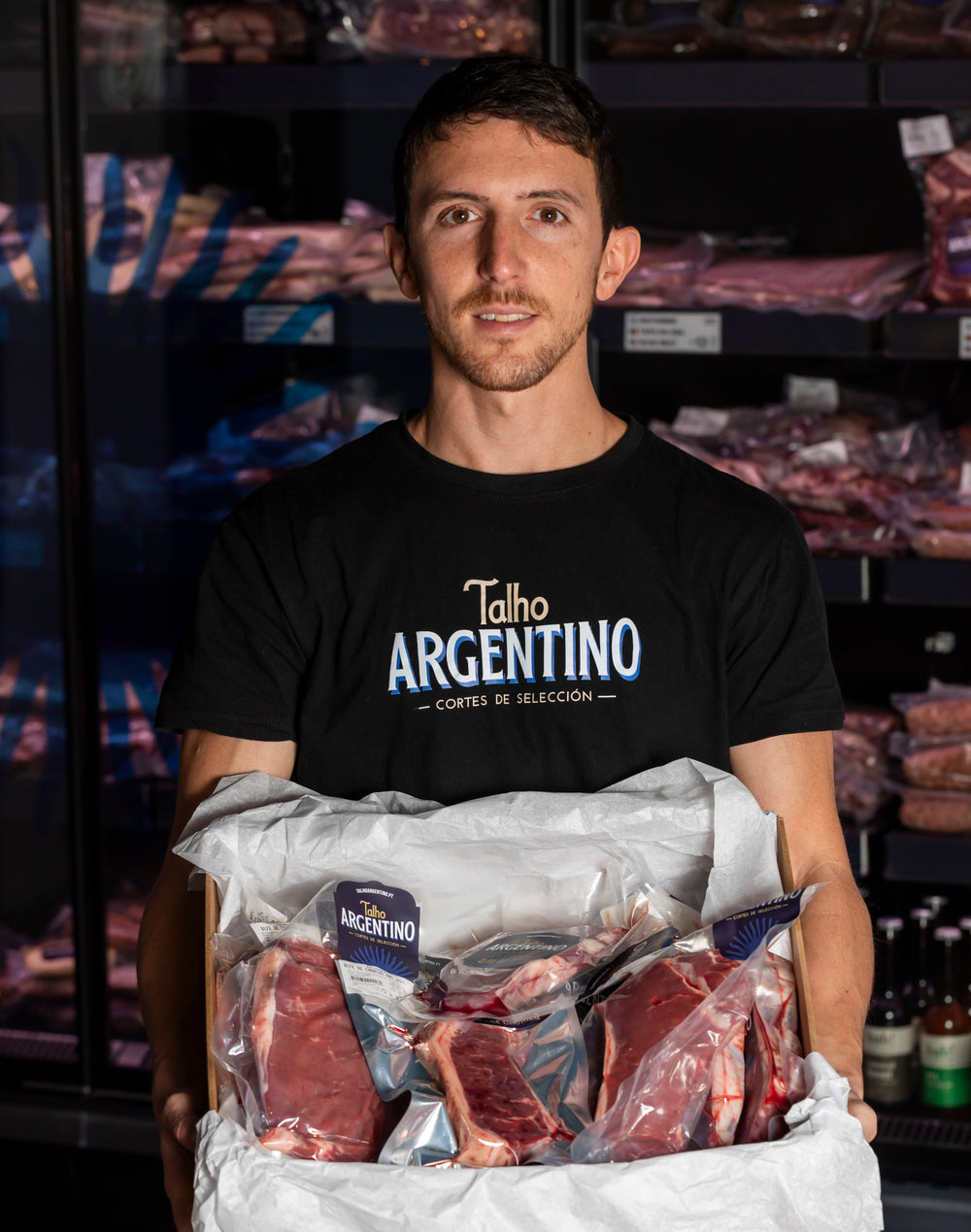 Personne en t-shirt Talho Argentino tenant une boîte de morceaux emballés sous vide
